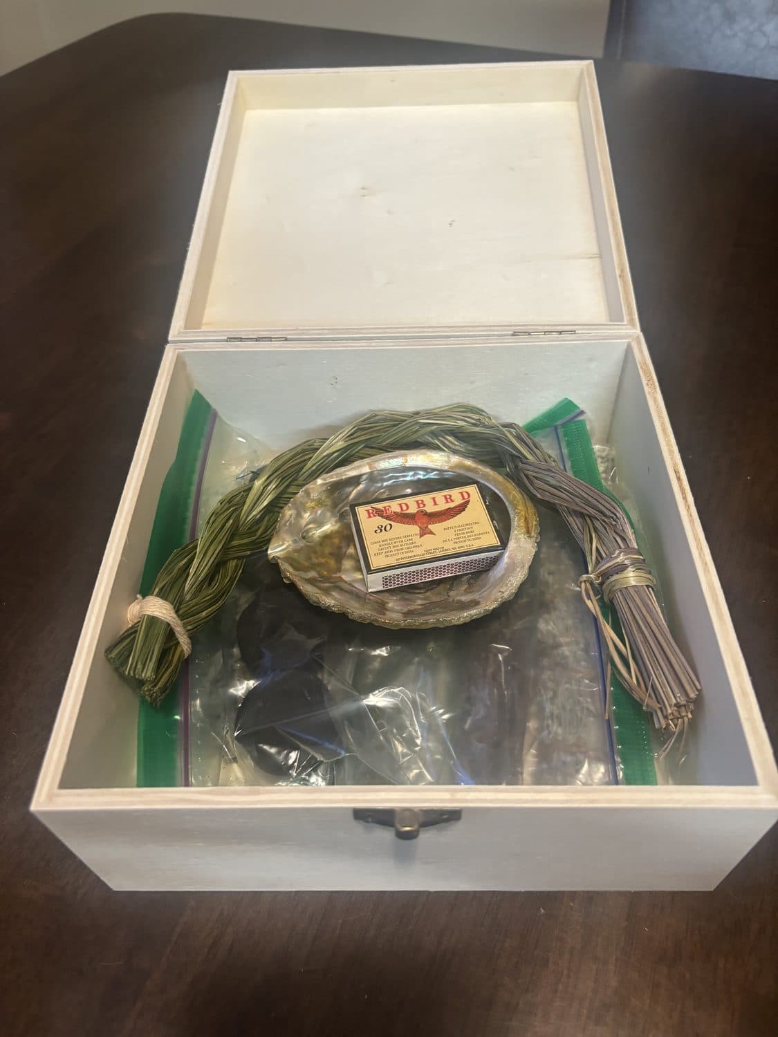 A wooden box holding braided sweetgrass, sage, and an abalone shell